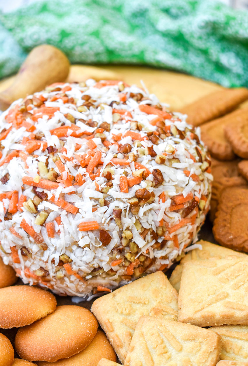 a carrot cake cheese ball on a wooden cutting board surrounded by cookies