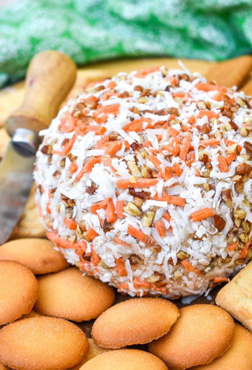 a carrot cake cheese ball on a wooden cutting board surrounded by cookies