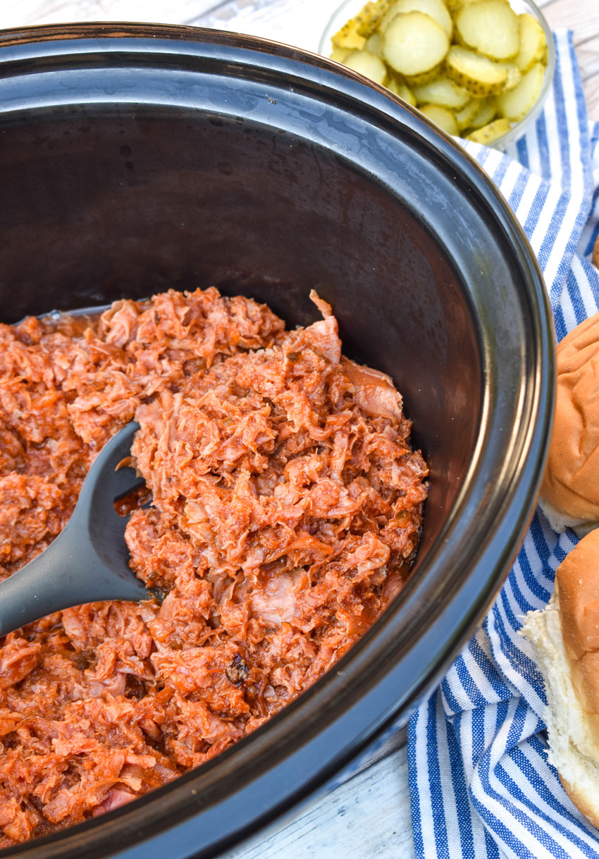 a spoon scooping shaved ham barbecue out of the black bowl of a crockpot
