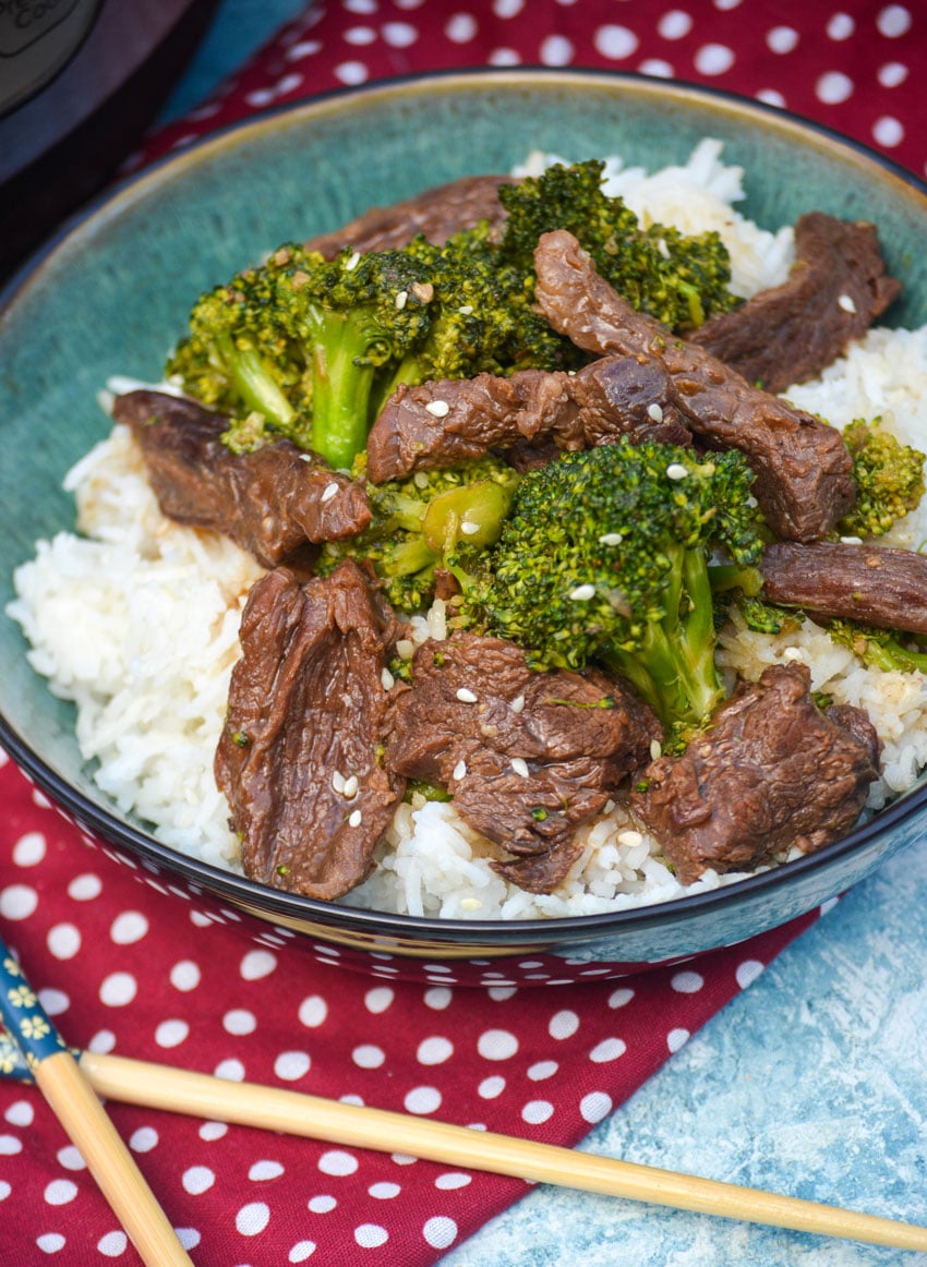 instant pot beef and broccoli in a green bowl next to a pair of wooden chopsticks 