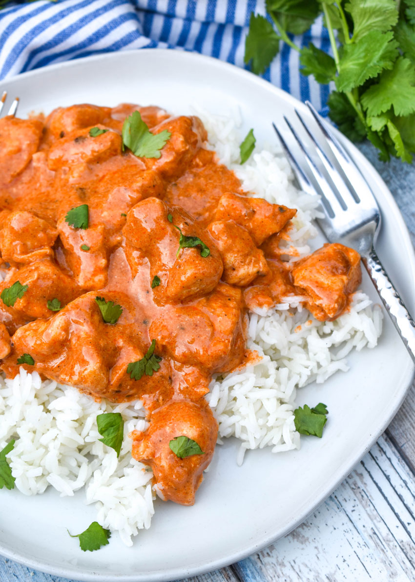 a silver fork resting on a white plate filled with crockpot butter chicken over rice