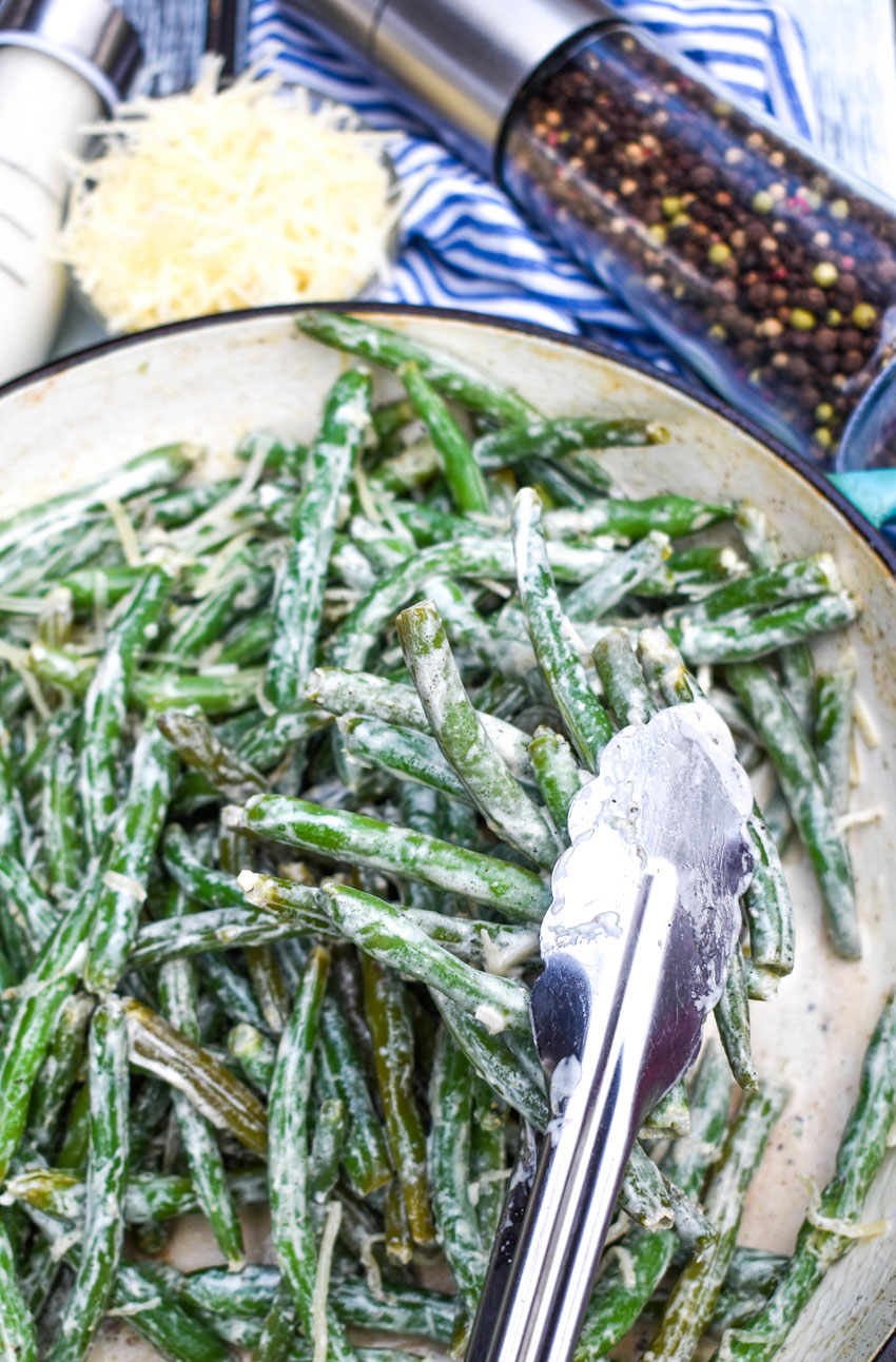 silver tongs in a skillet filled with caesar green beans