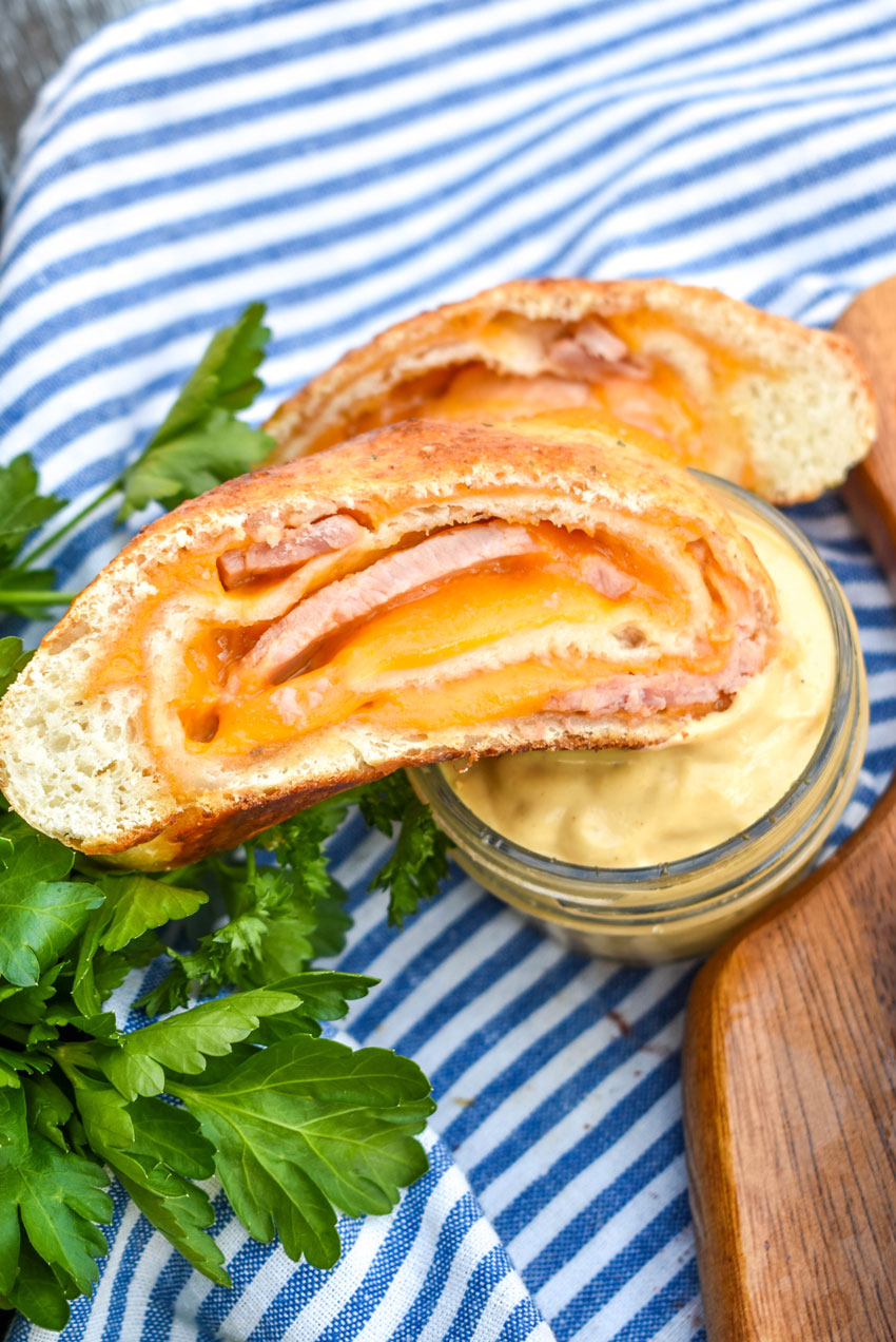 a slice of ham and cheese stromboli being dipped into a glass jar filled with honey mustard