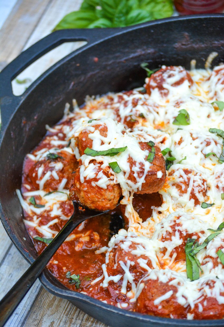 a black spoon in a cheesy meatball parmesan skillet