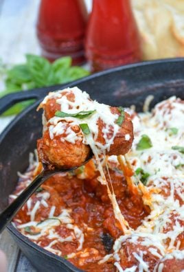 a black spoon holding up cheesy tomato sauce covered meatballs