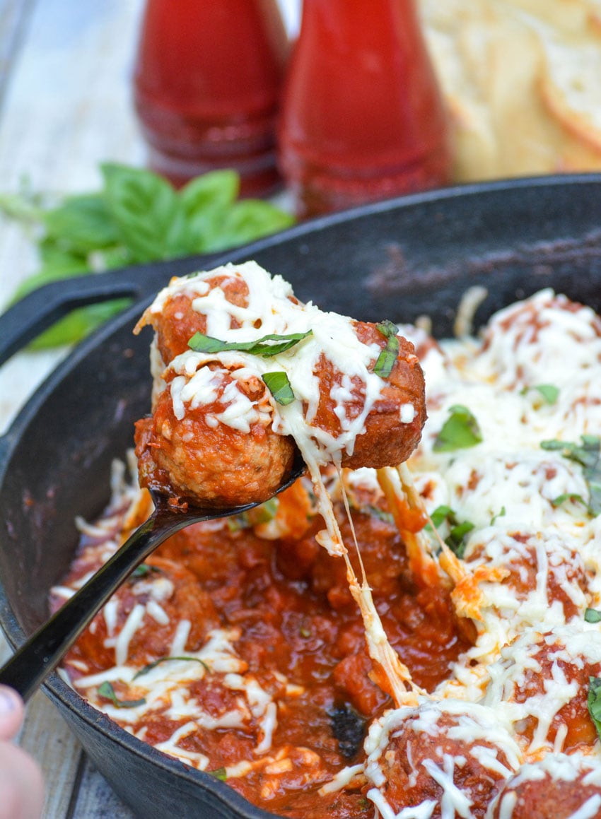 a black spoon holding up cheesy tomato sauce covered meatballs