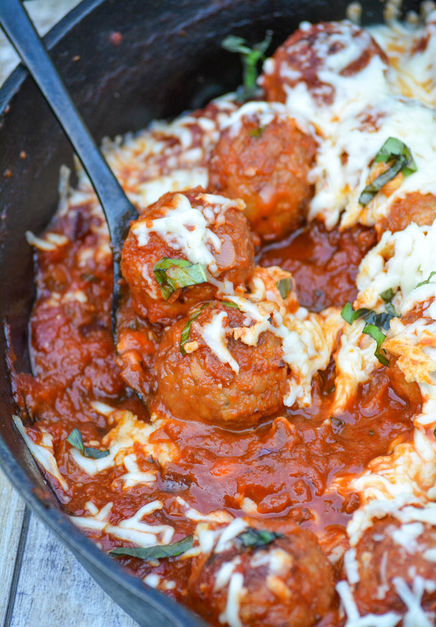 a black spoon scooping a serving out of a meatball parmesan skillet