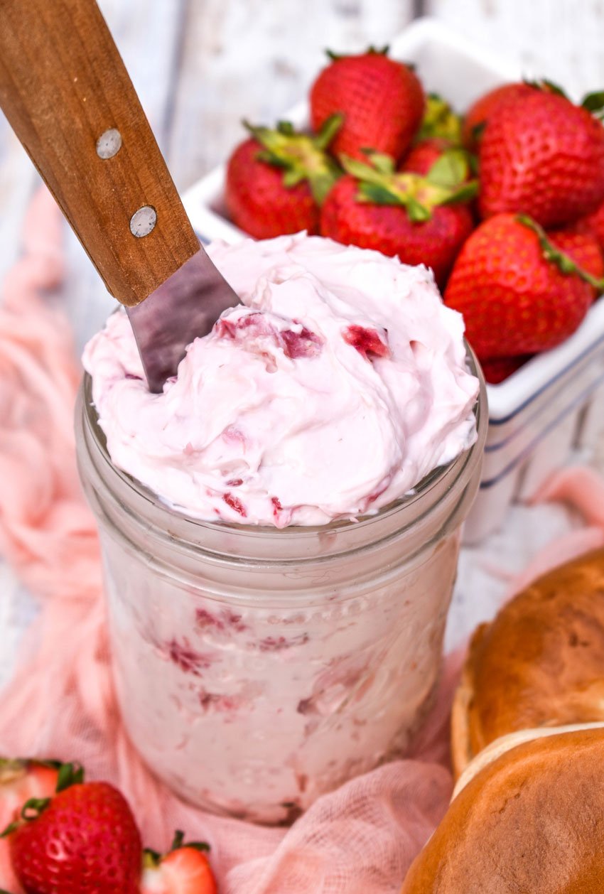 a wooden spreader stuck in a glass jar filled with easy strawberry cream cheese recipe