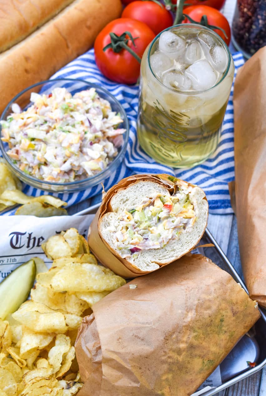chopped sub sandwich wrapped in brown parchment paper on a metal tray with chips