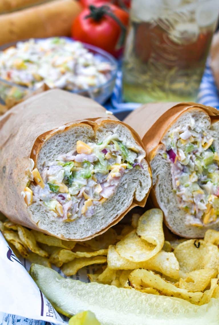 two halves of a chopped sub sandwich on a metal serving tray with potato chips