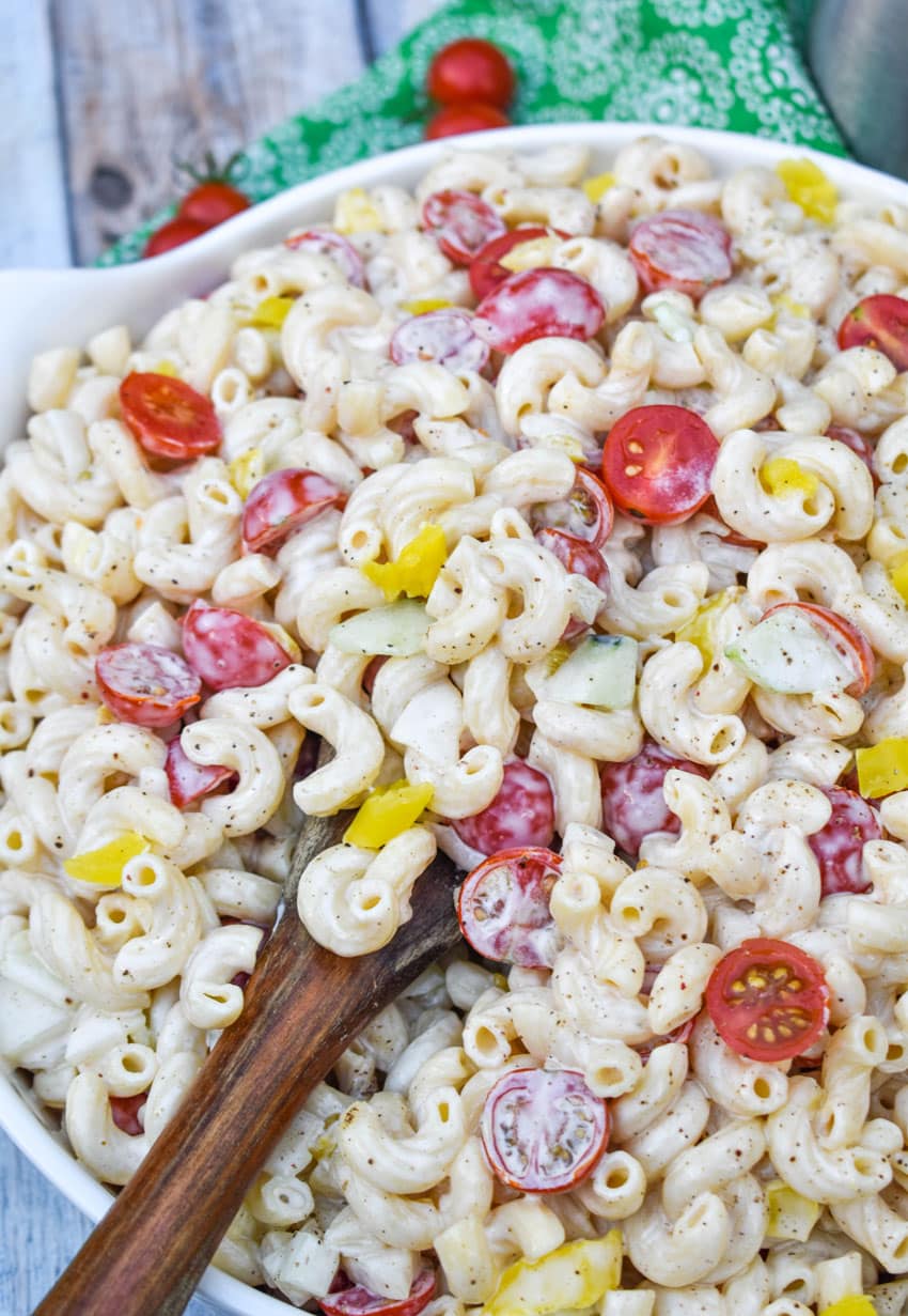 a wooden spoon in a serving bowl filled with creamy macaroni salad recipe