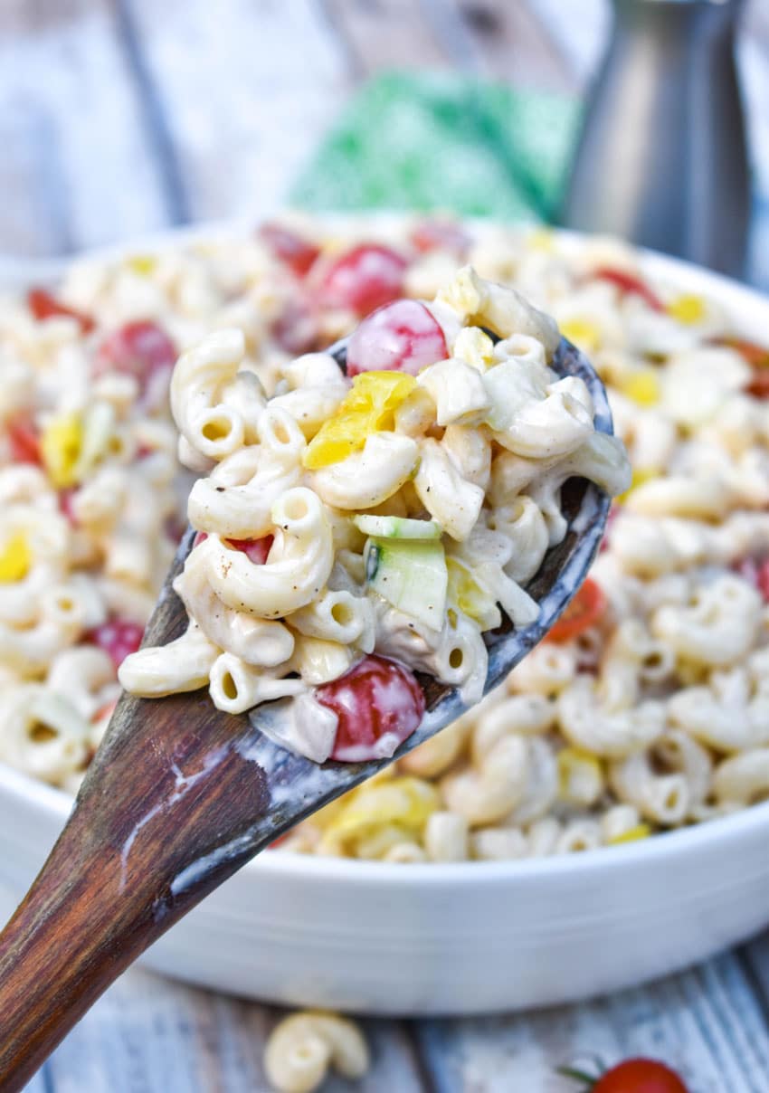 a wooden spoon holding up a scoop of creamy macaroni salad recipe