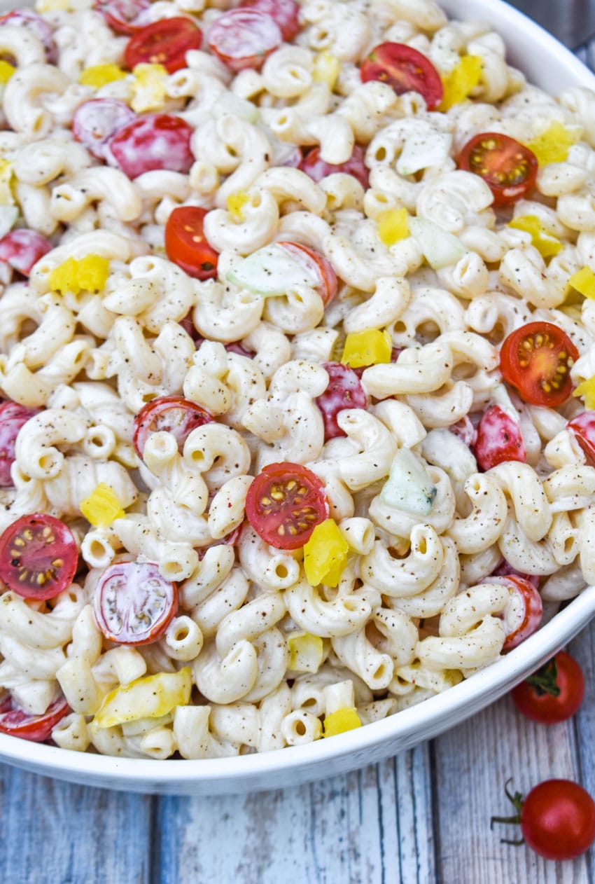 creamy macaroni salad with cucumber and tomato in a white serving bowl