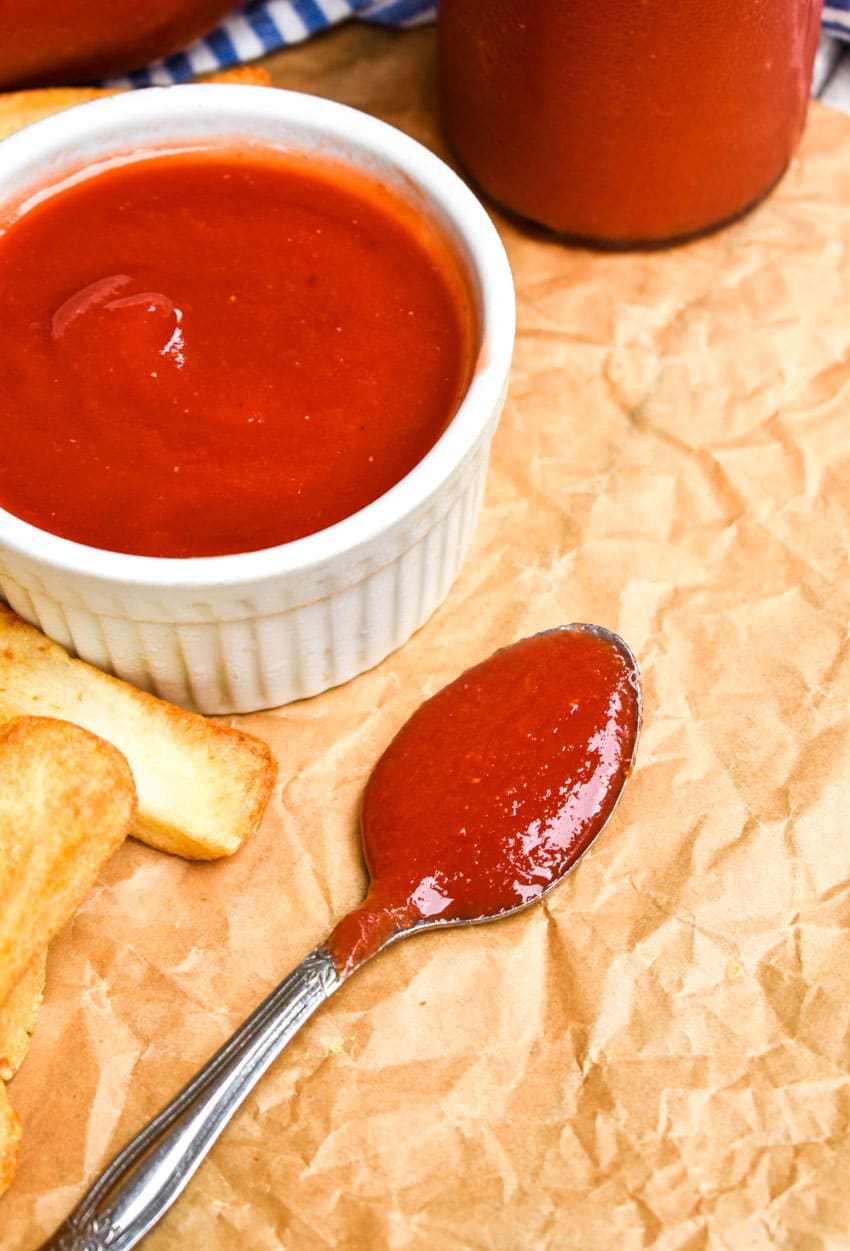 a silver spoon holding homemade ketchup resting on brown parchment paper
