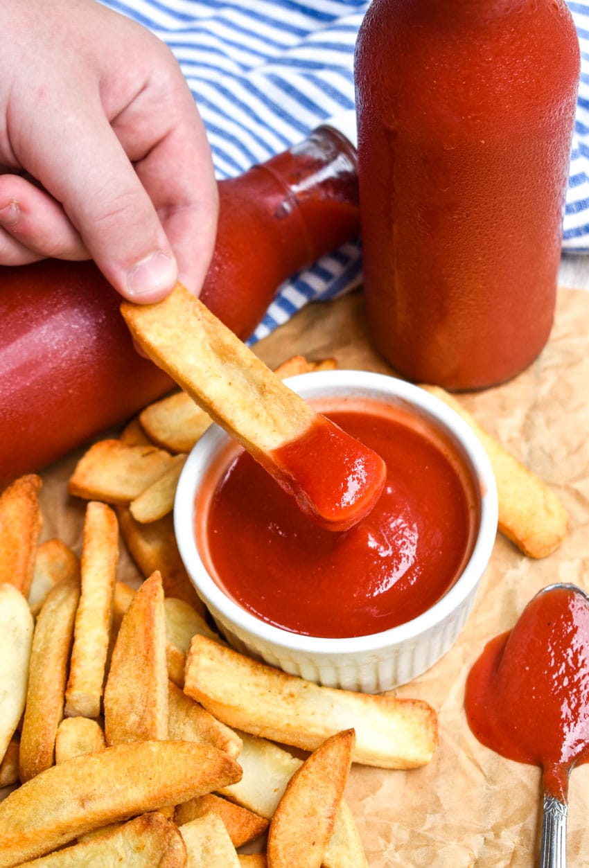 a hand holding up a french fry covered in easy homemade ketchup