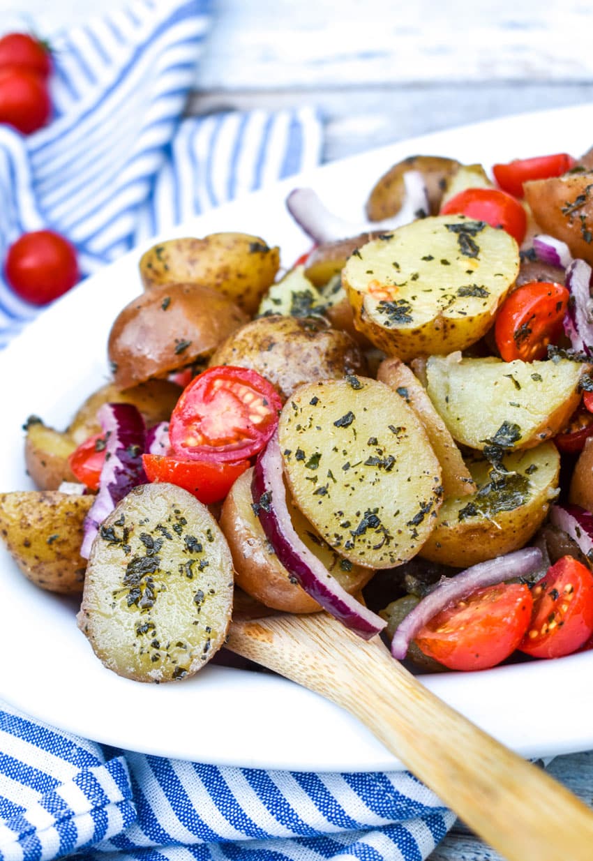 a wooden spoon stuck in a bowl of italian potato salad with tomatoes