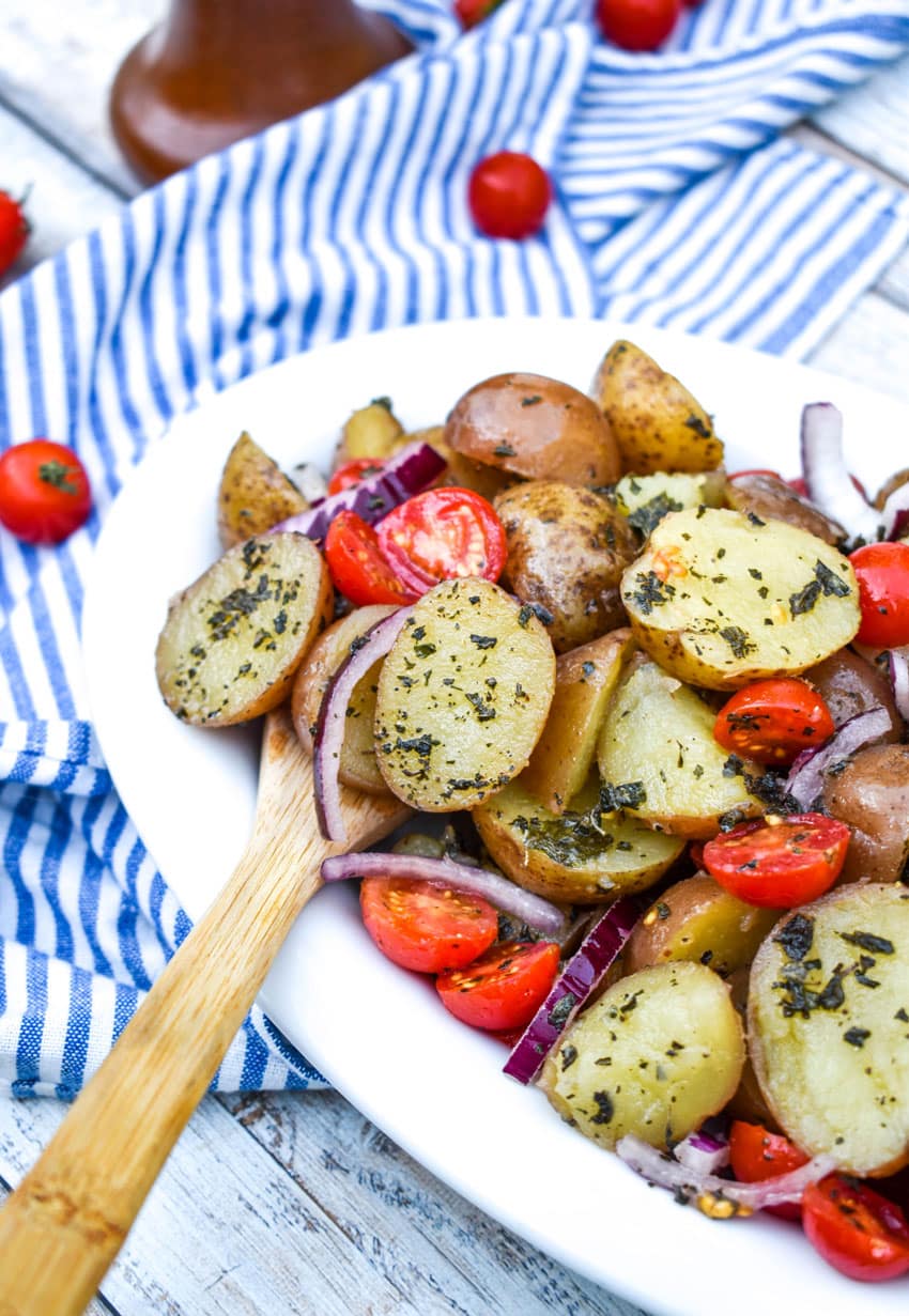 a wooden spoon stuck in a bowl of italian potato salad with tomatoes