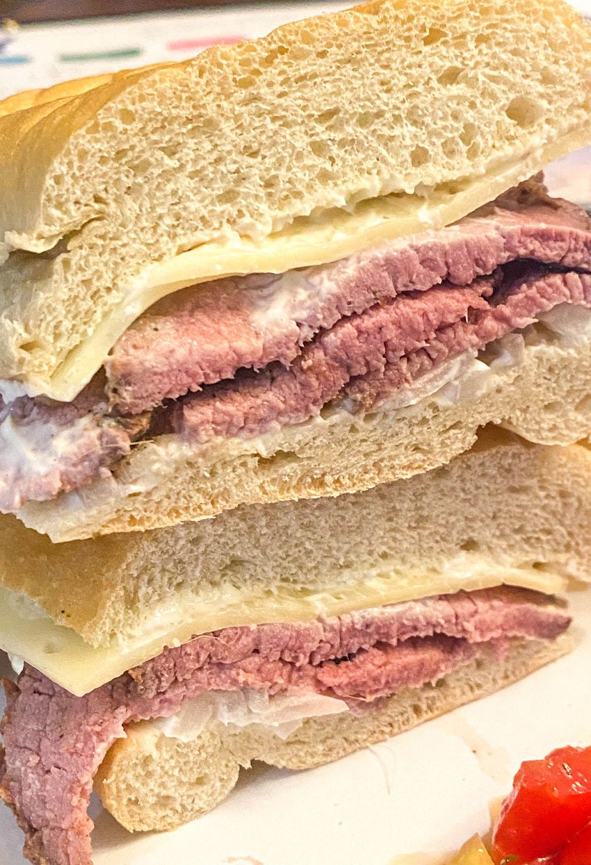 two halves of a smoked roast beef sandwich stacked on top of each other on a white plate