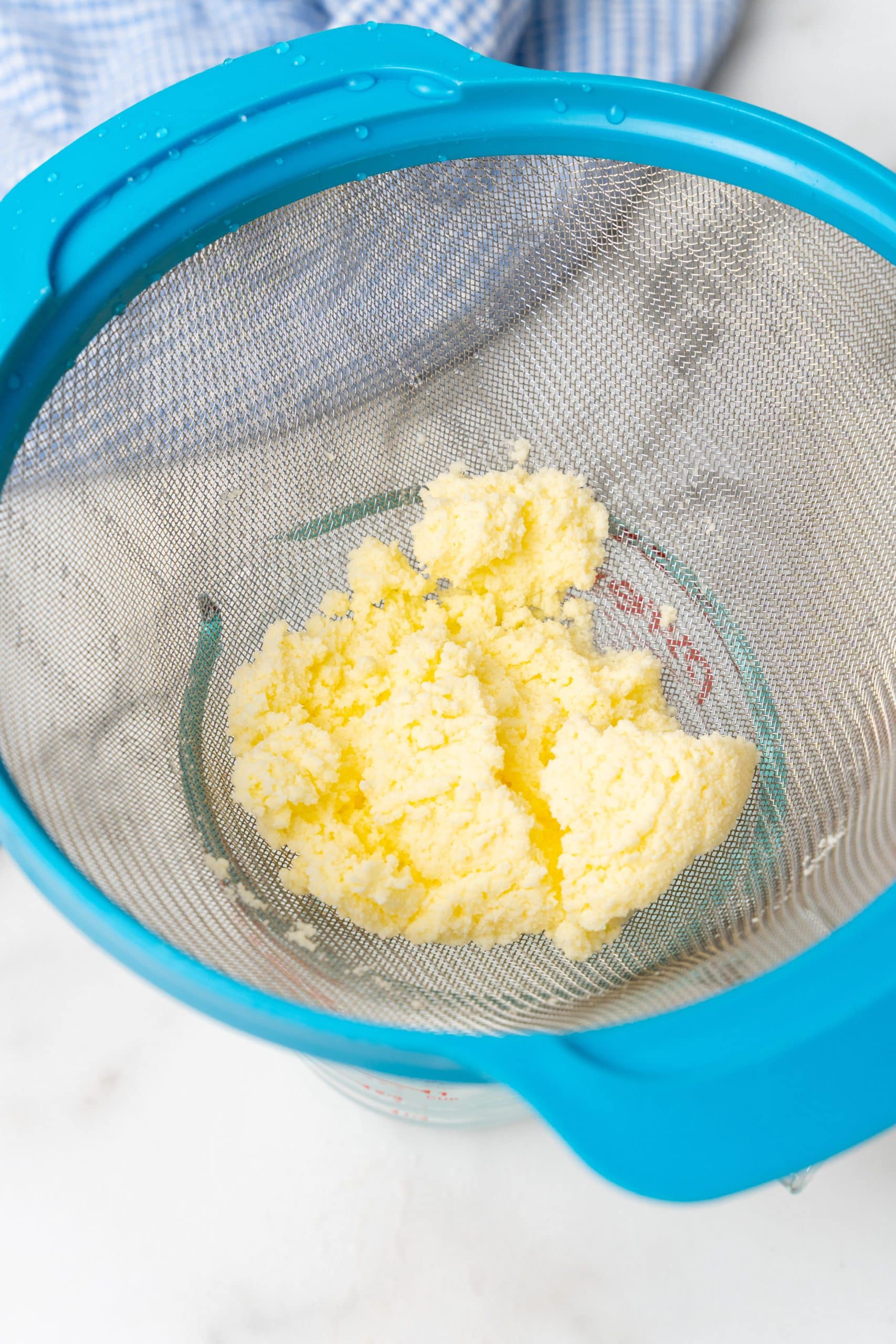 homemade butter in a mesh strainer set over a glass bowl