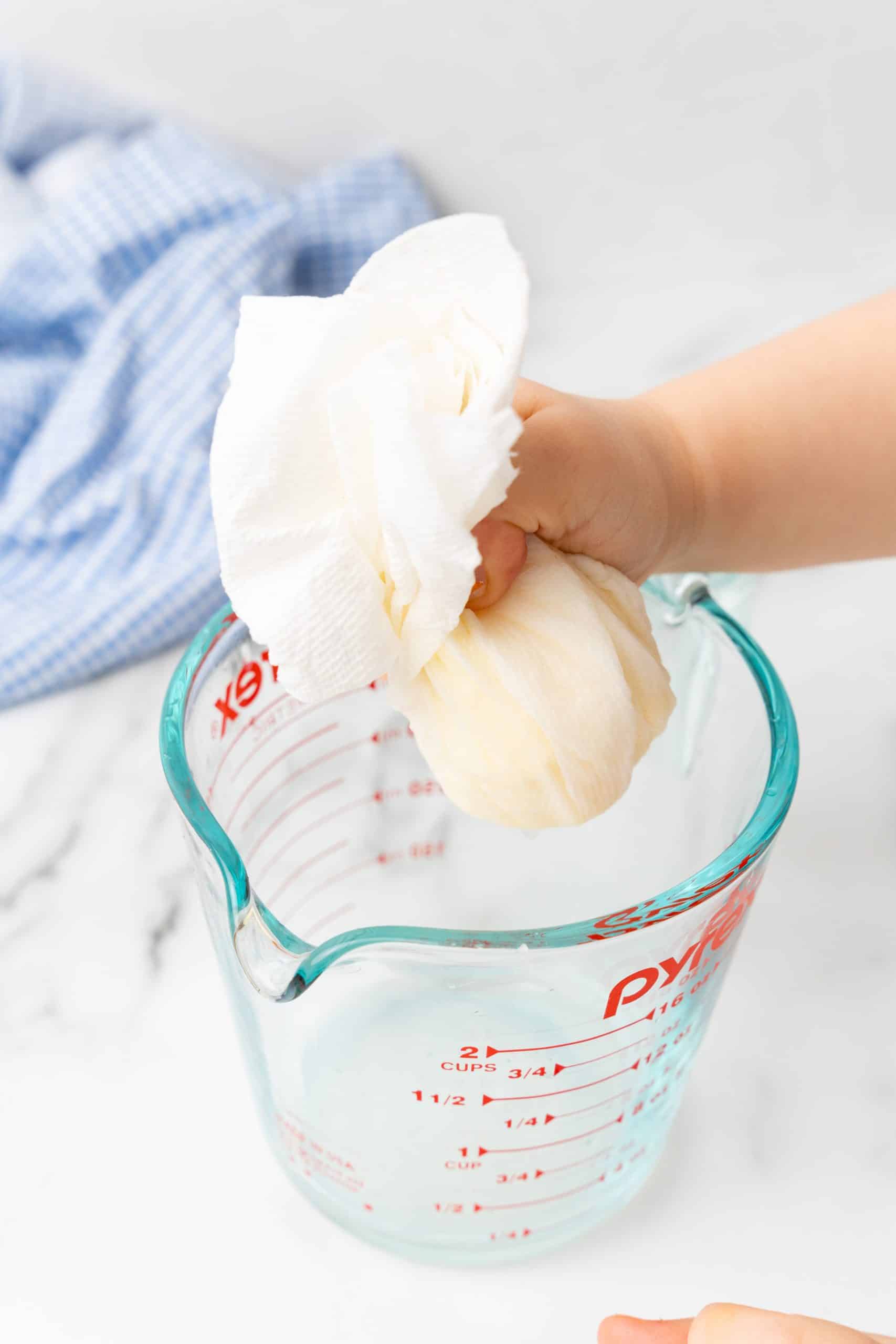 a small hand squeezing butter in a paper towel over a glass measuring cup