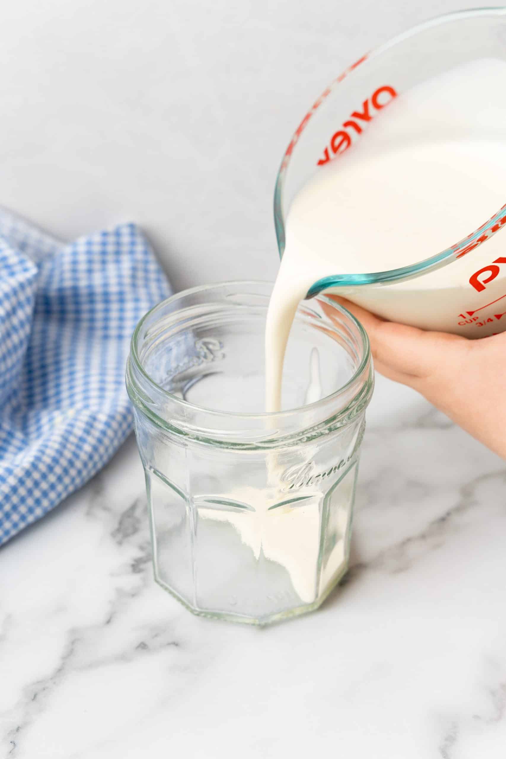cream being poured into a glass jar from a measuring cup