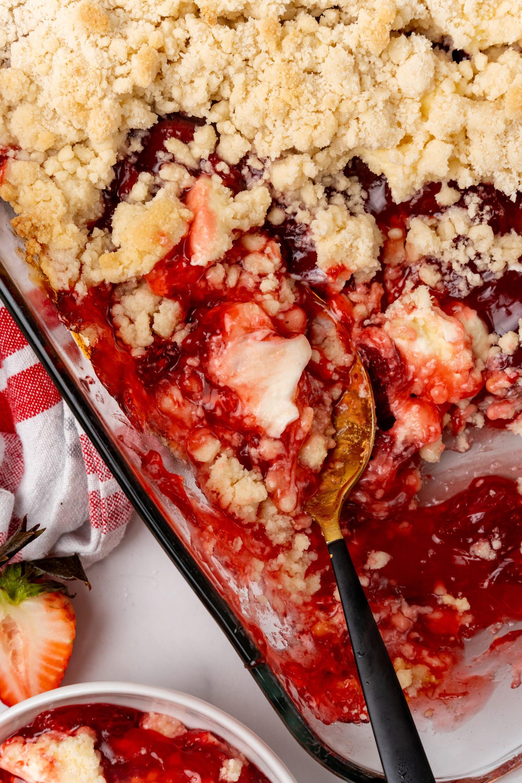 a spoon resting in a glass baking dish filled with baked strawberry dump cake