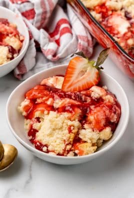 strawberry cheesecake dump cake served in a white bowl with a fresh strawberry on top