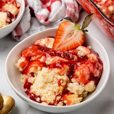 strawberry cheesecake dump cake served in a white bowl with a fresh strawberry on top
