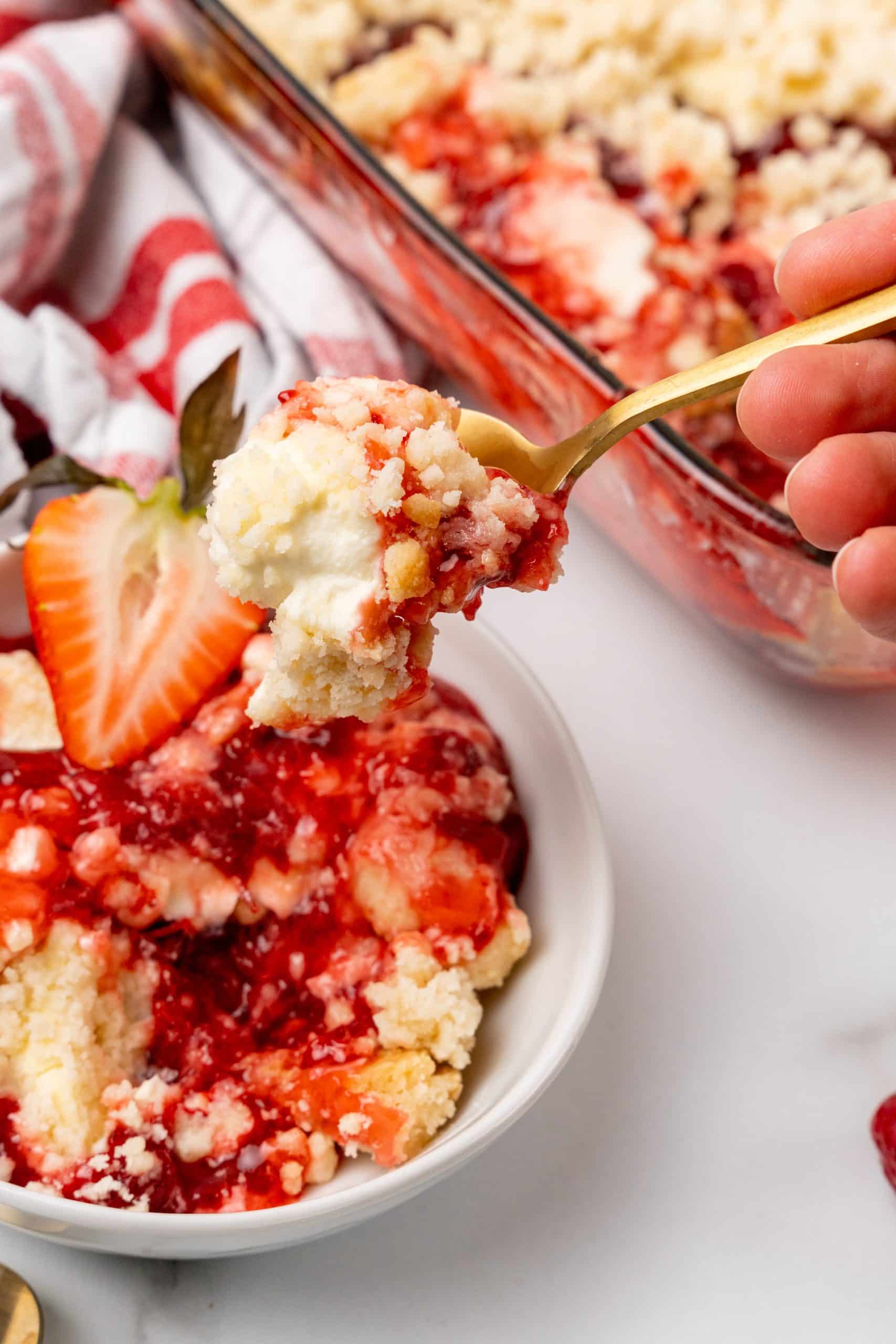 a gold spoon holding up a scoop of baked dump cake with strawberries