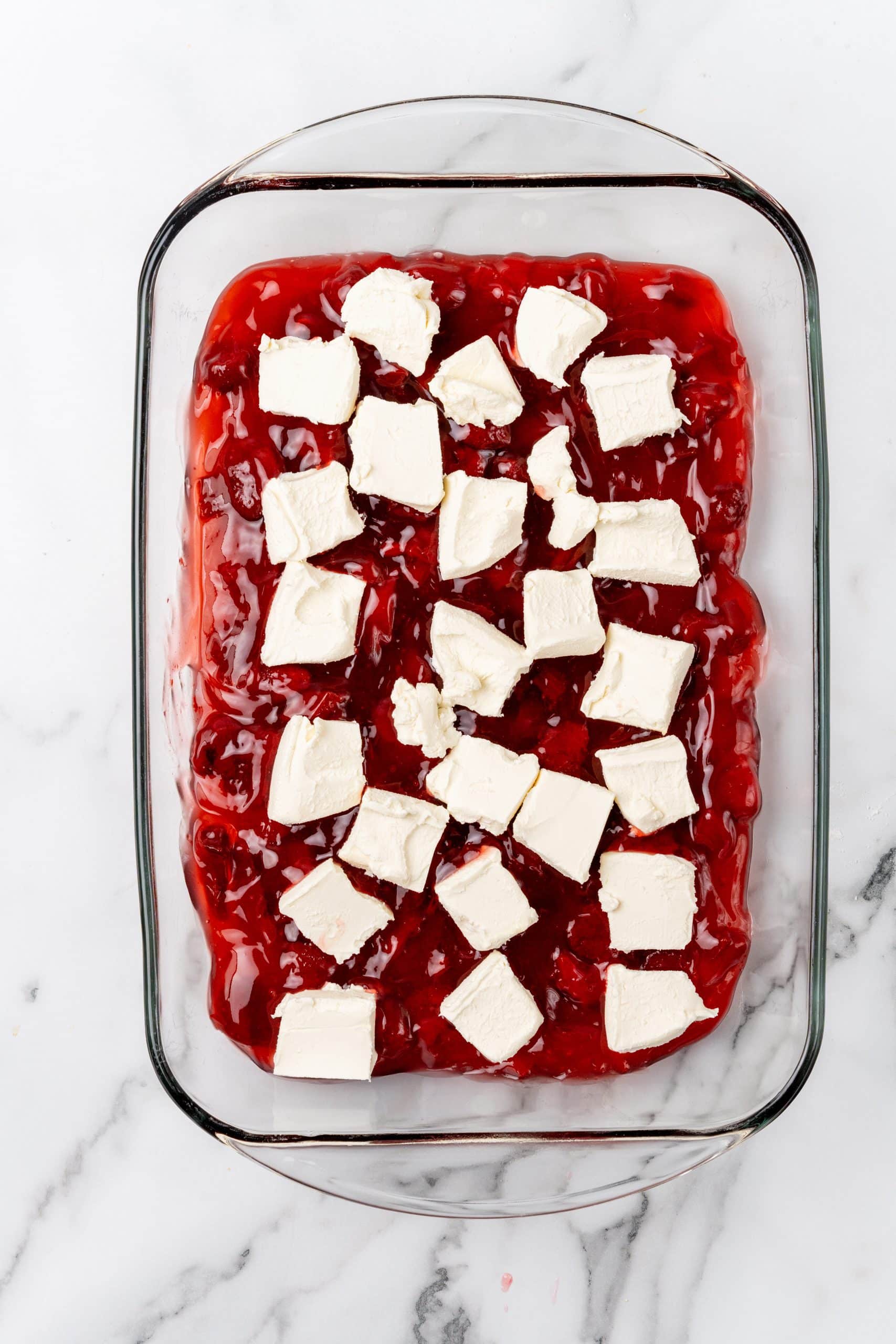 slices of cream cheese laid out on top of strawberry pie filling in a glass baking dish