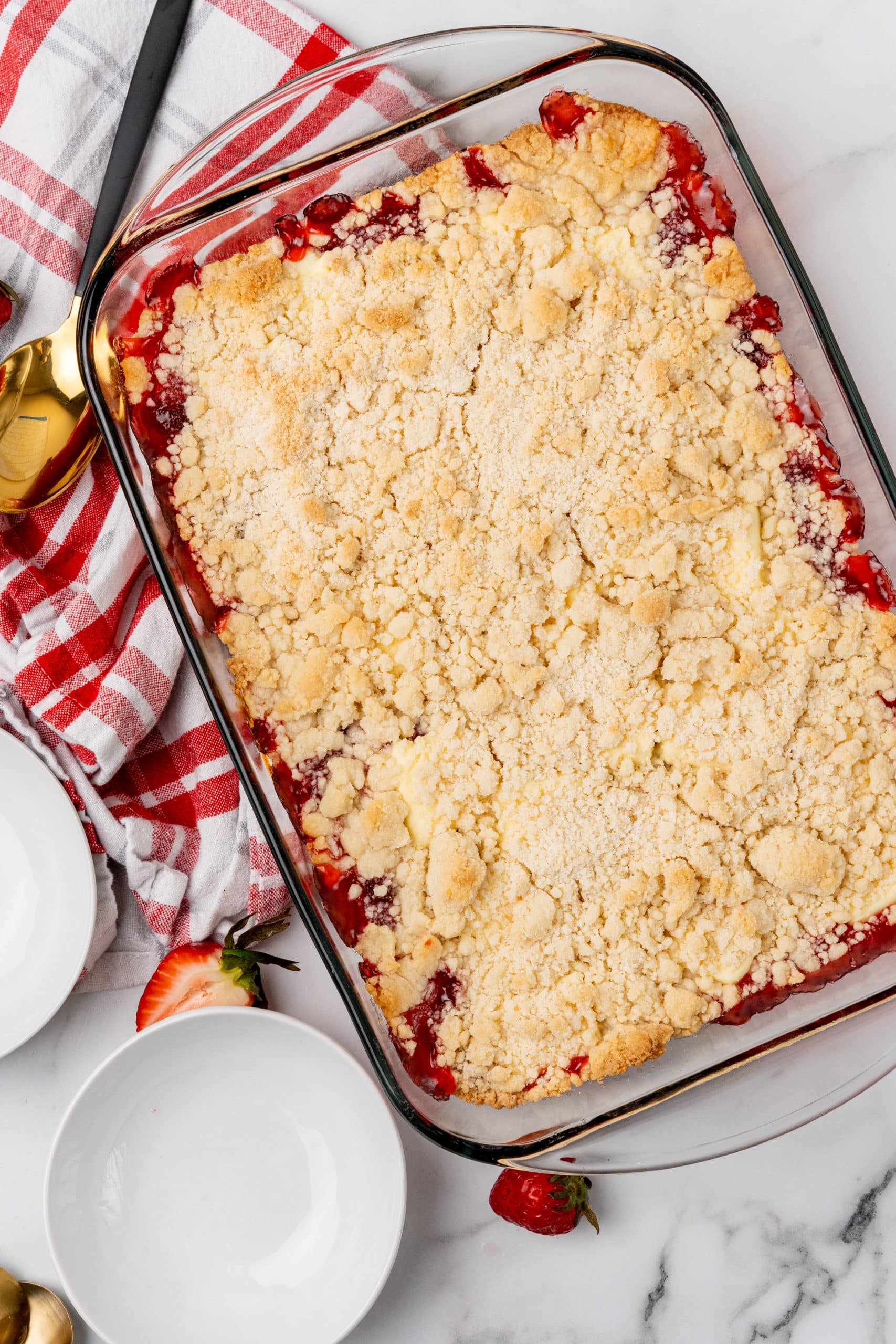 a strawberry cheesecake dump cake in a glass baking dish with white dessert plates on the side