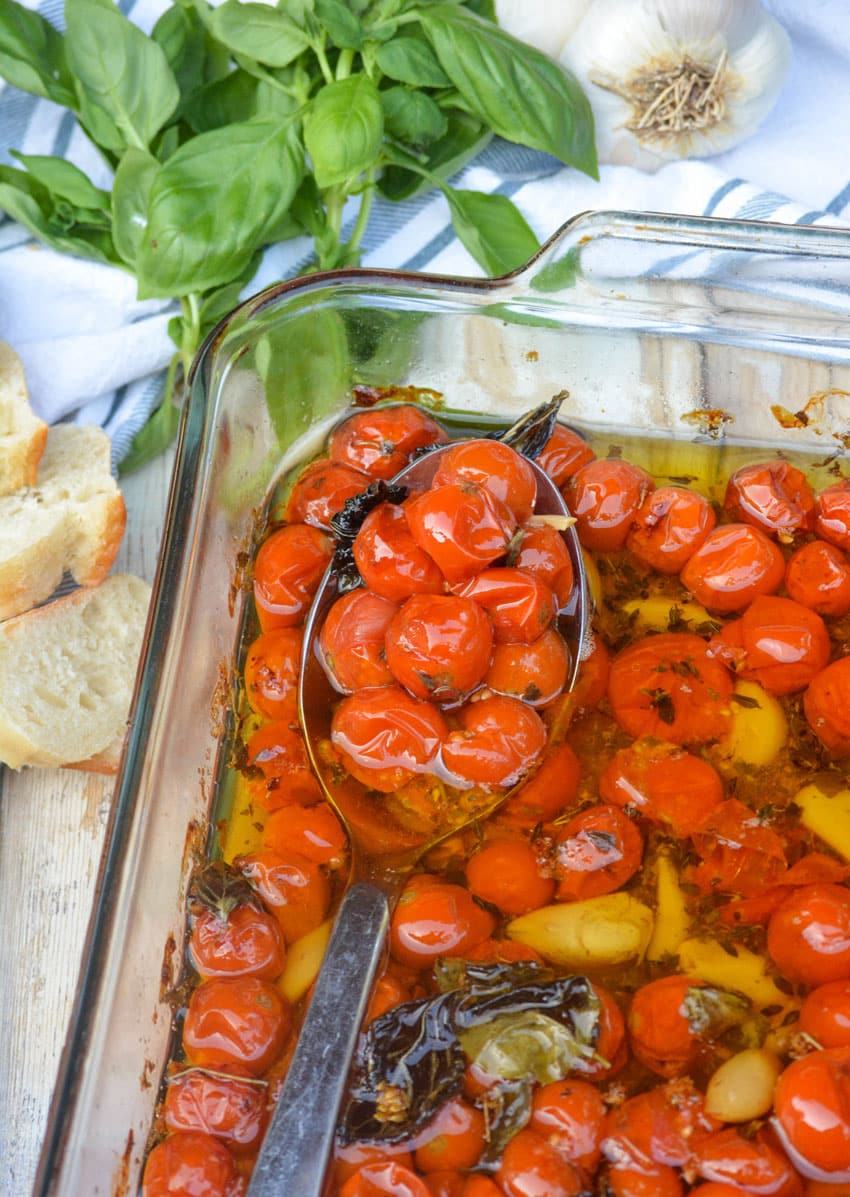 a slotted silver spoon in a baking dish filled with quick tomato confit recipe