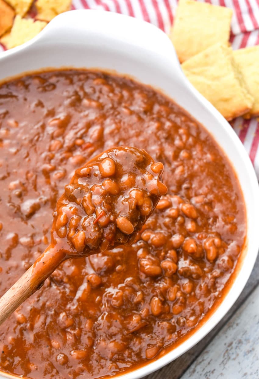 a wooden spoon holding up a scoop of baked beans with brisket