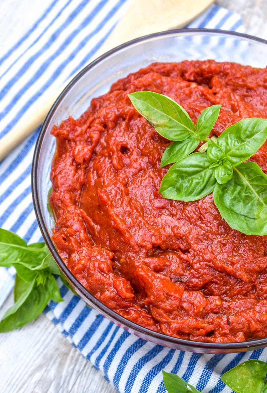 homemade tomato paste in a glass bowl topped with fresh basil leaves