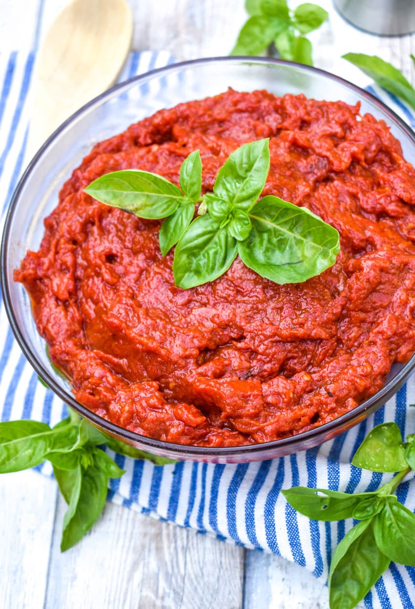 homemade tomato paste in a glass bowl topped with fresh basil leaves