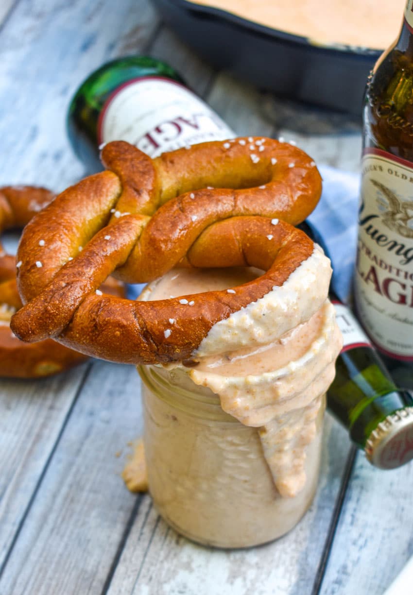 a soft pretzel covered in smoked beer cheese dip resting on top of a glass jar