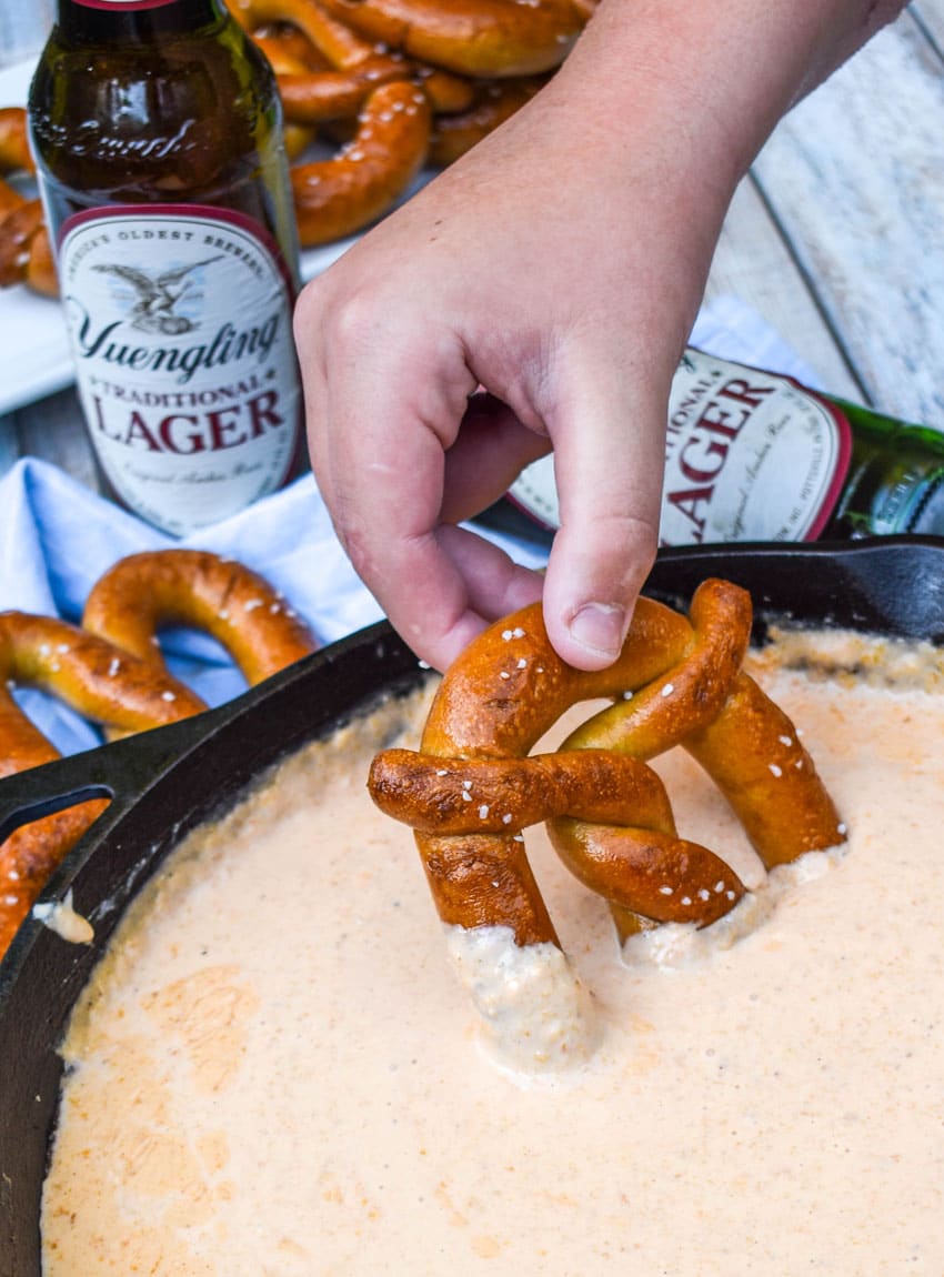 a hand dipping a soft pretzel into a skillet of smoked beer cheese dip
