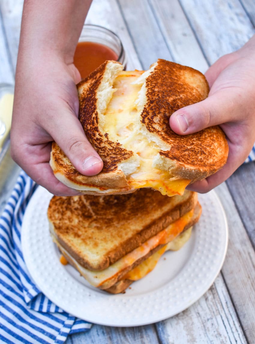 two hands pulling apart an extra cheesy three cheese grilled cheese sandwich
