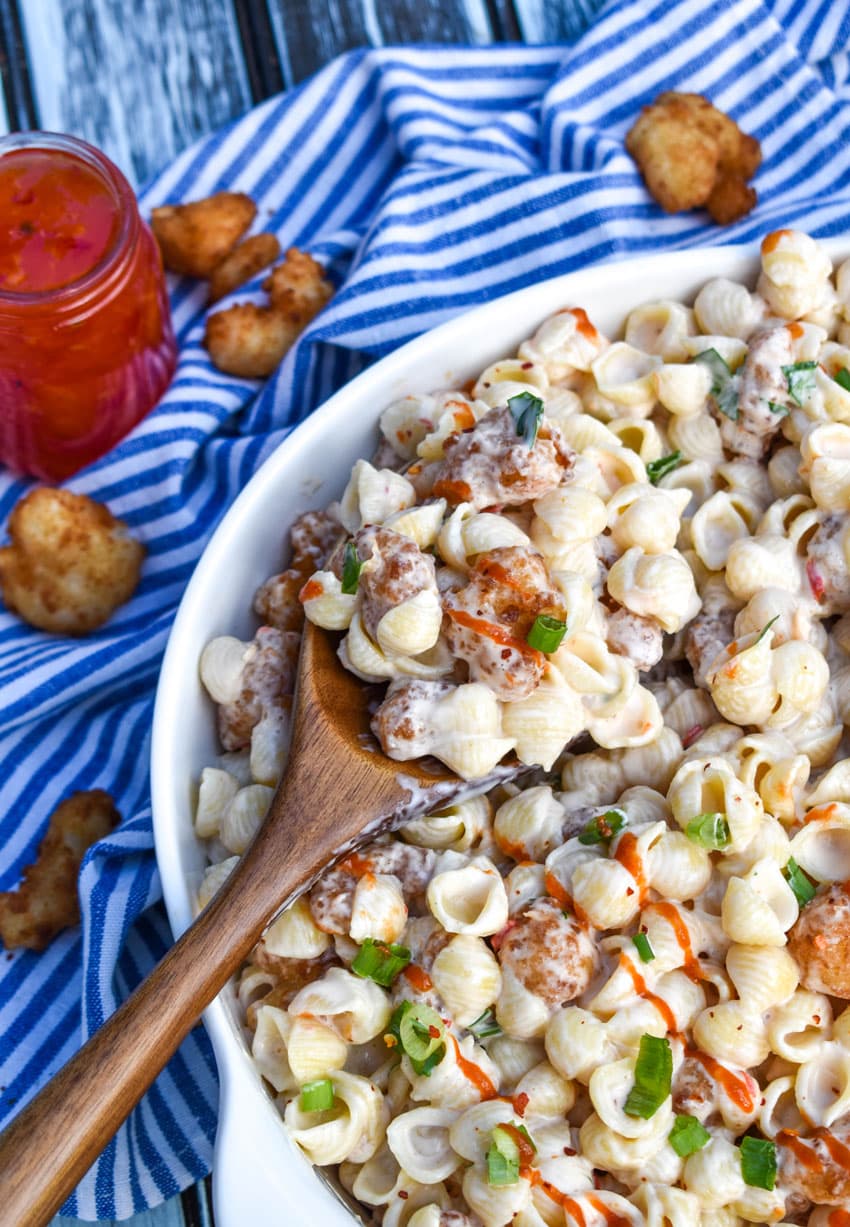 a wooden spoon stuck in a serving bowl filled with creamy pasta salad with popcorn shrimp