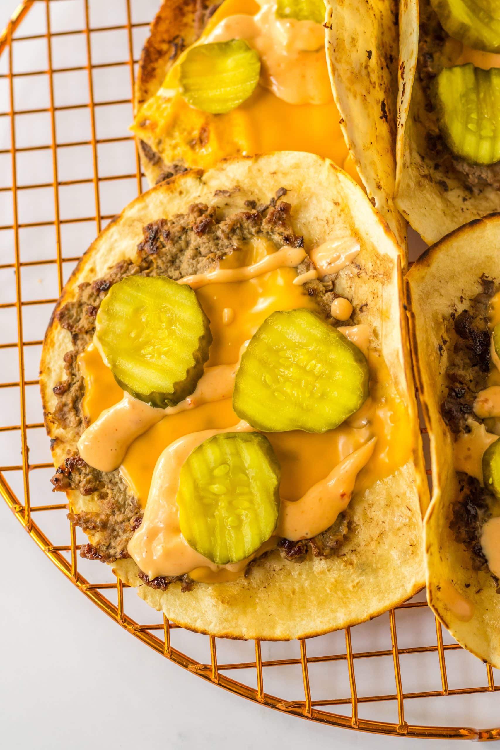 a smash taco topped with melted cheese and sliced pickles on a wire rack