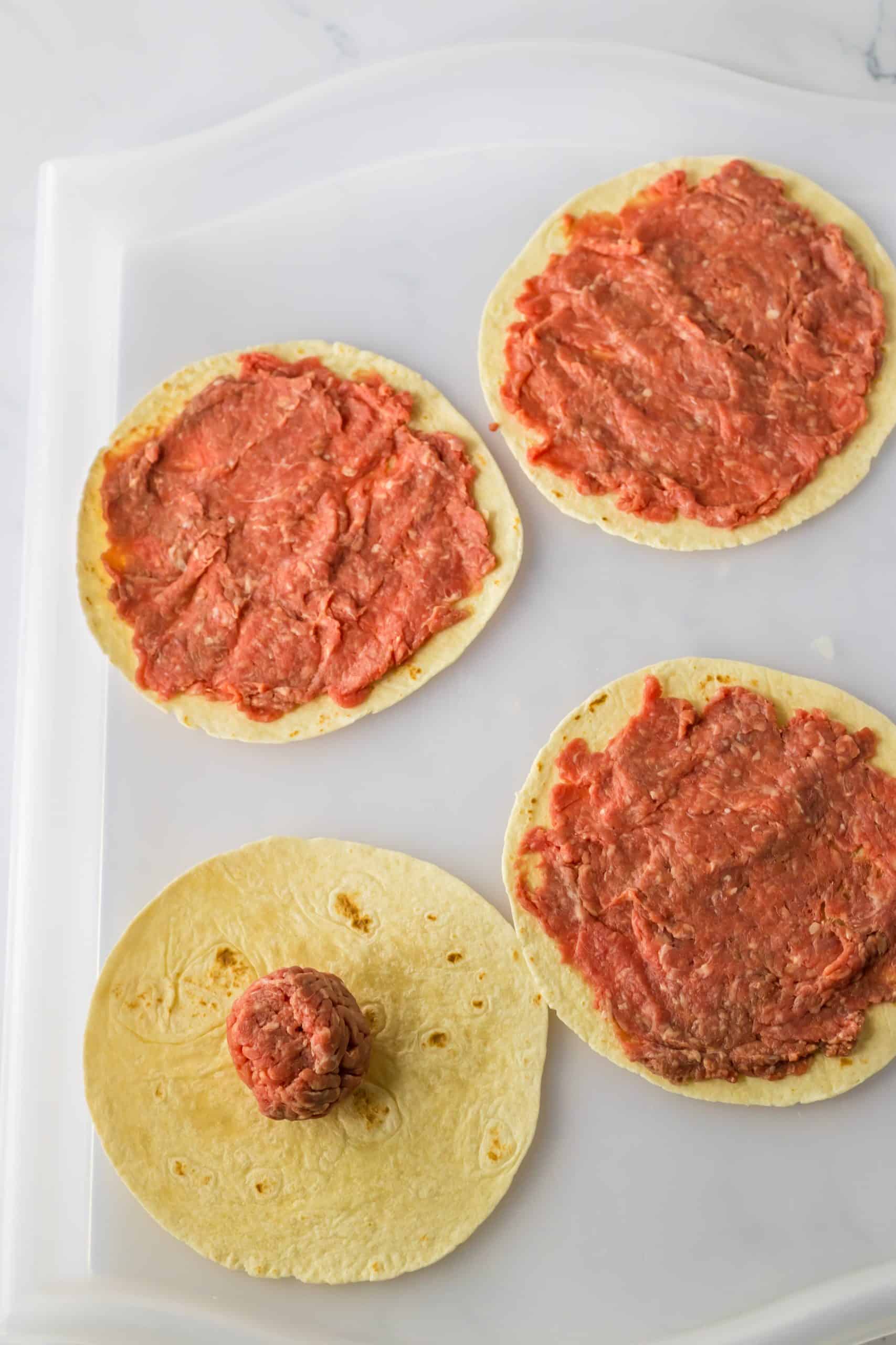 raw ground beef flattened and spread on tortillas in a thin layer