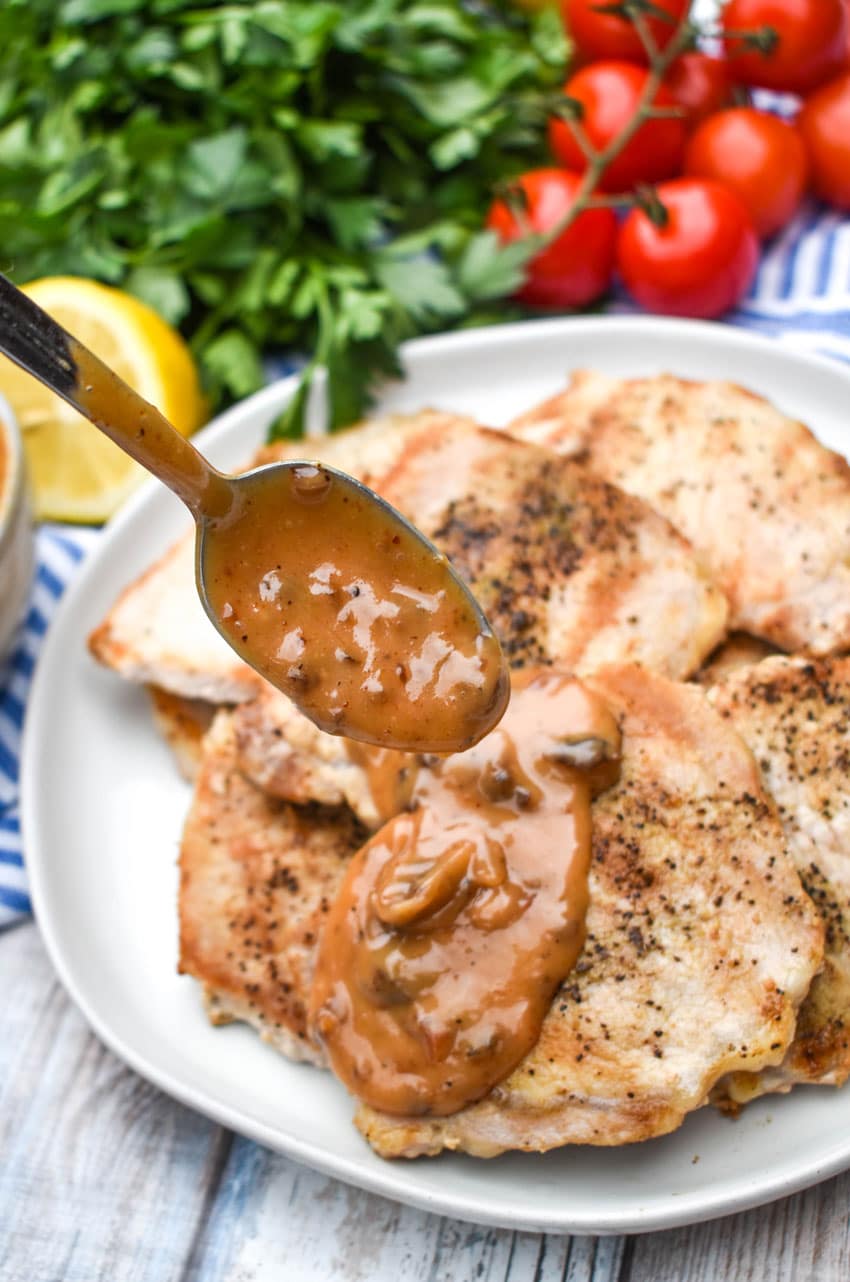 a spoon drizzling creamy tomato chutney sauce over Greek pork chops on a white plate