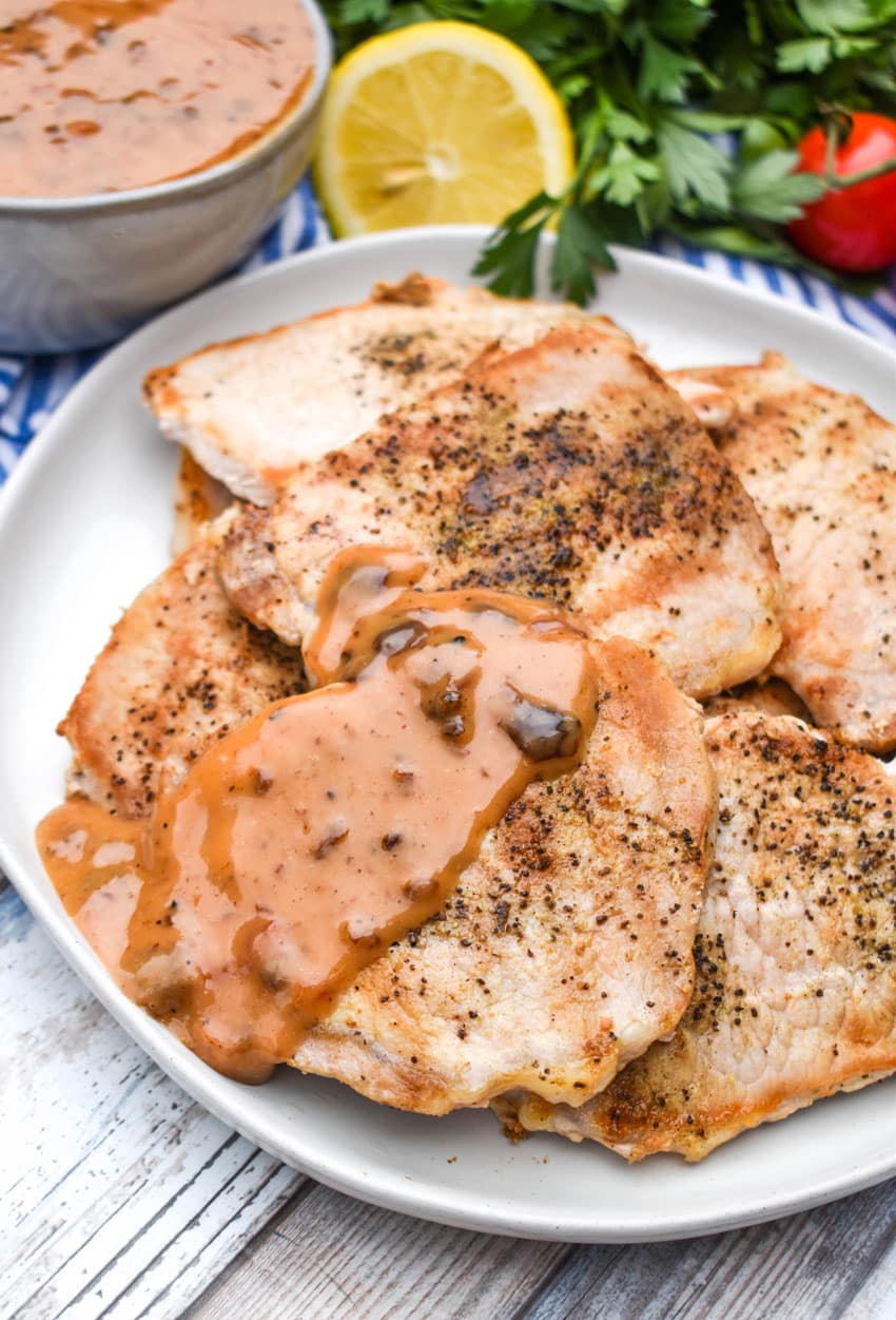 creamy tomato chutney sauce topped Greek season pork chops on a white serving plate