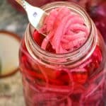 a silver fork scooping pickled red onions out of a large glass mason jar