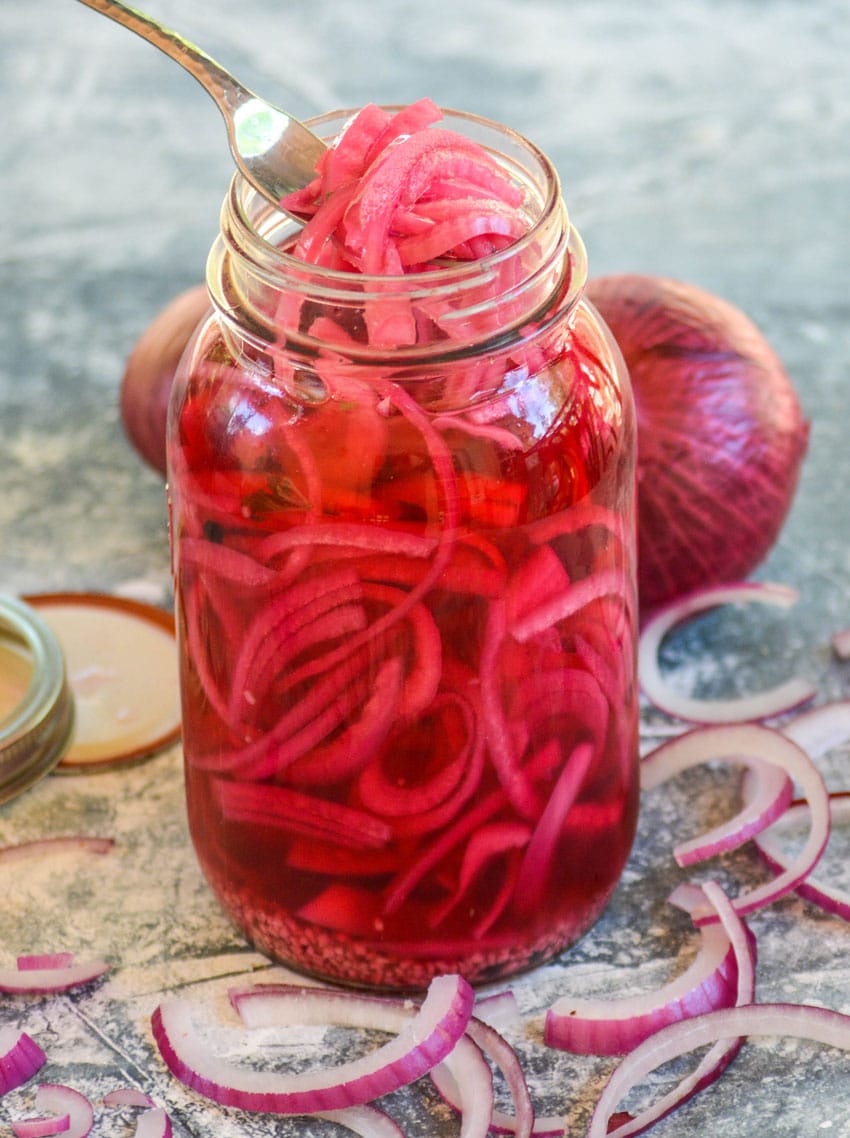 a silver fork scooping pickled red onions out of a large glass mason jar