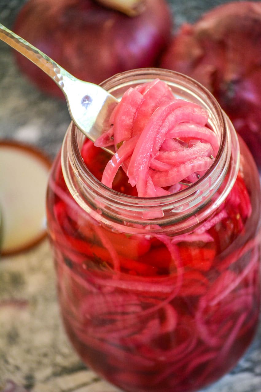 a silver fork scooping pickled red onions out of a large glass mason jar