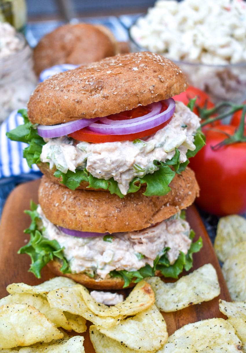 two smoked chicken salad sandwiches stacked on top of each other and surrounded by potato chips