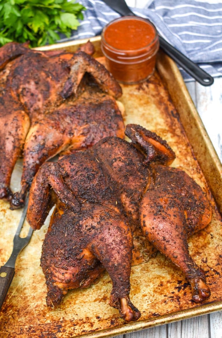 two smoked spatchcock chickens on a metal sheet pan