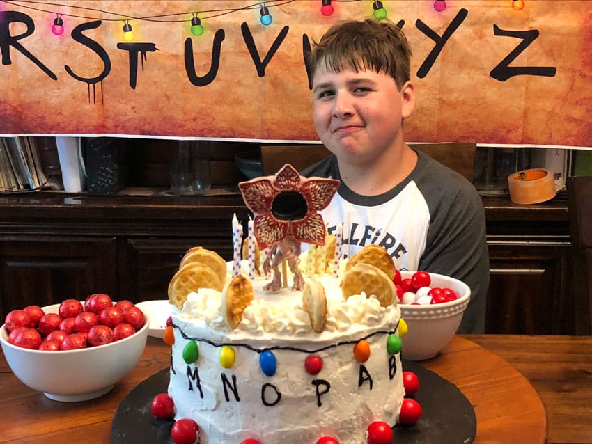 a boy seated at a kitchen table behind a stranger things themed birthday cake