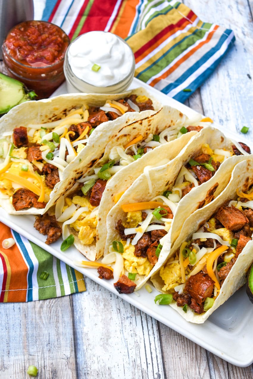 a row of breakfast tacos arranged on a white serving platter